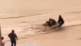 Matka přechází se svým dítětem zaplavenou silnici