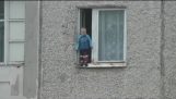 Ein Kind 2 Jahre alt, der auf dem Rand des Fensters auf der 8. Etage