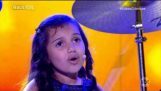 O fetiță în vârstă de șapte ani joacă toxicitate la tobe și cântă în același timp
